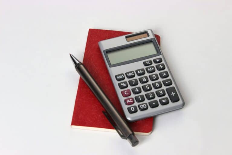 Calculadora, cuadernos y bolígrafos sobre una mesa de trabajo mientras se calcula el presupuesto de marketing de un negocio pequeño